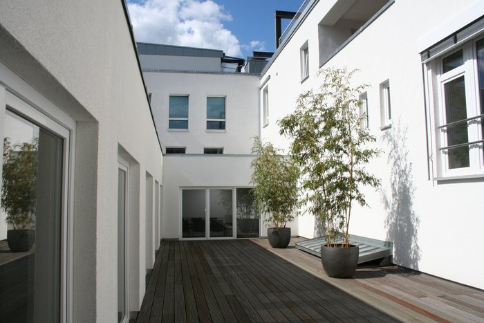 Innenhof mit Holzdeck, Pflanzkübeln und weißen Fassaden