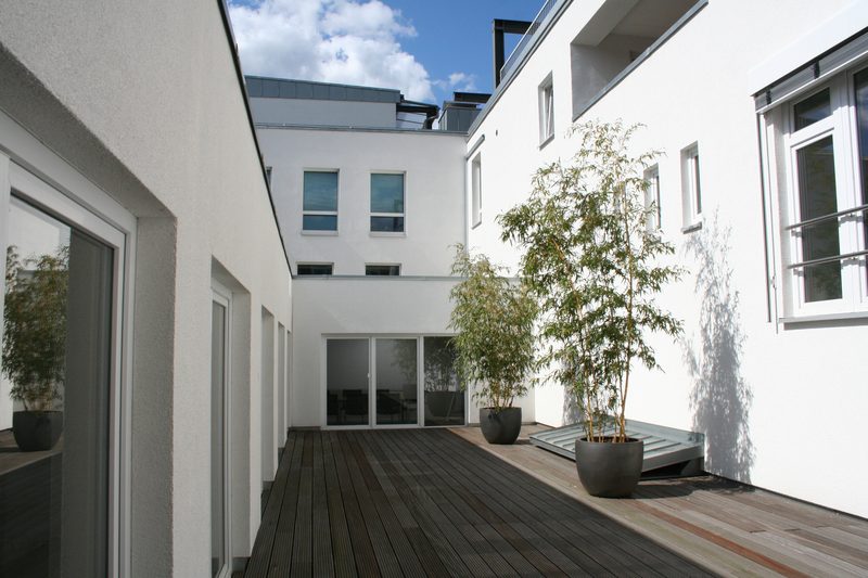Innenhof mit Holzdeck, Pflanzkübeln und weißen Fassaden